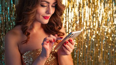 Parlak altın bir arka planda telefon kullanan genç bir kadın.