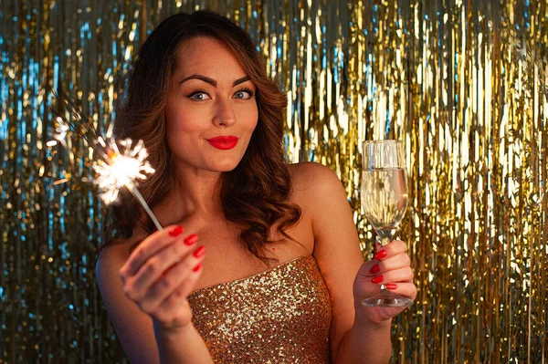Giovane donna beve champagne e tenendo una scintilla su uno sfondo oro brillante, messa a fuoco selettiva — Foto Stock