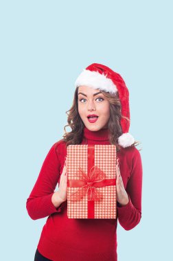 Kırmızı elbiseli ve elinde hediyeyle Noel Baba şapkalı bir kadının dikey portresi.