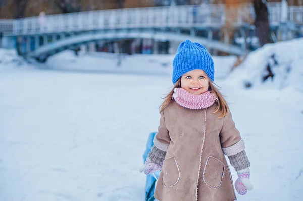 Portrait of a little girl with a sleigh on a background of snow in the park — Photo