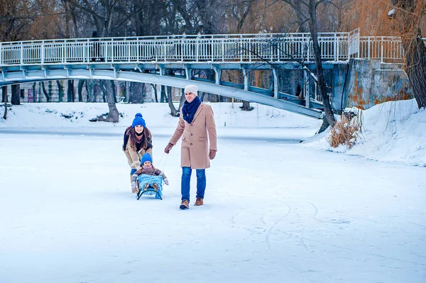 Parents ride their daughter on a sleigh, frozen lake against the background of the bridge — Photo