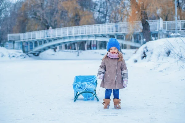 Portrait of a little girl with a sleigh on a background of snow in the park — Photo