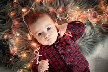 Ekose gömlekli bebek çelengin yanında uzanmış kameraya bakıyor.