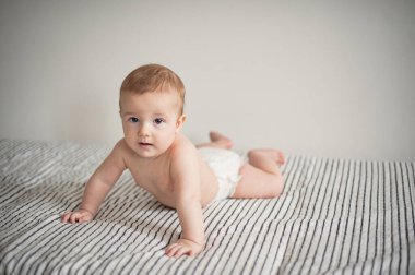 Çizgili bir battaniyeye uzanmış bebek bezi giymiş bir çocuğun portresi.