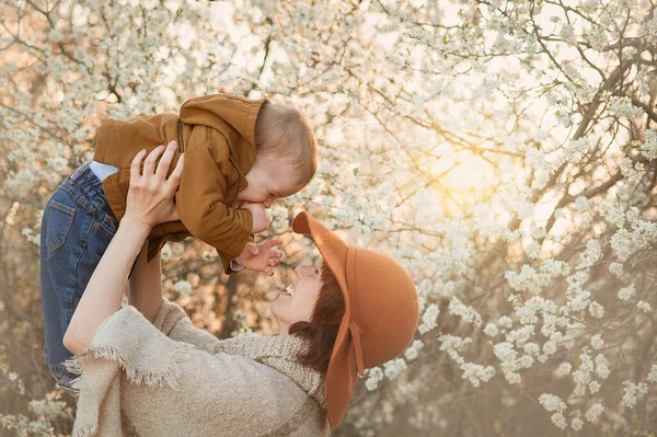 Moeder houdt de baby tegen de achtergrond van bloeiende bomen Stockafbeelding