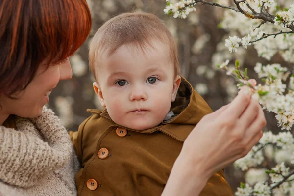 Moeder houdt de baby tegen de achtergrond van bloeiende bomen Rechtenvrije Stockafbeeldingen