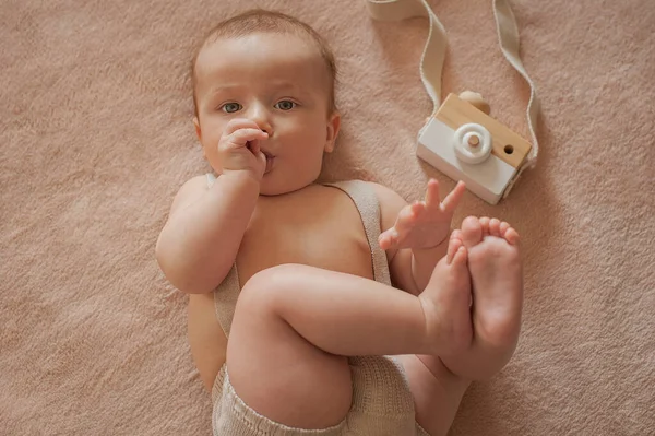 Baby met een houten camera ligt op een beige achtergrond De baby zuigt zijn duim Stockfoto