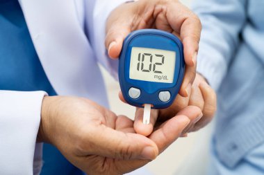 Diyabet tedavisinde kan şekeri seviyesini kontrol etmek için dijital glikoz ölçer kullanan Asyalı doktor.
