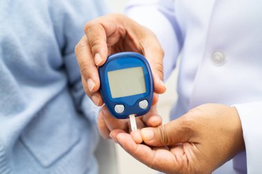 Diyabet tedavisinde kan şekeri seviyesini kontrol etmek için dijital glikoz ölçer kullanan Asyalı doktor.