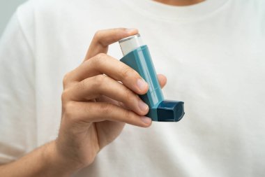 Astım ve kronik obstrüktif akciğer hastalığı COPD, Asyalı genç adam ölçülü doz solunum cihazı kullanıyor..