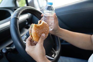 Asyalı kadın sürücü arabada hamburger ve patates kızartması yer, tehlikeli ve kaza riski taşır..