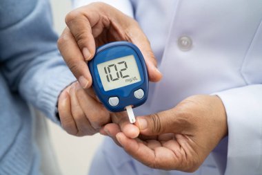 Diyabet tedavisinde kan şekeri seviyesini kontrol etmek için dijital glikoz ölçer kullanan Asyalı doktor.