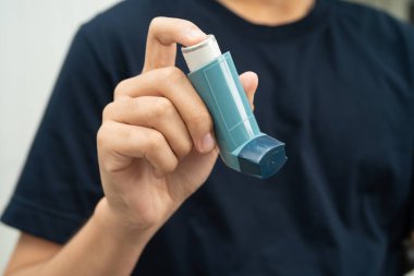 Astım ve kronik obstrüktif akciğer hastalığı COPD, Asyalı genç adam ölçülü doz solunum cihazı kullanıyor..
