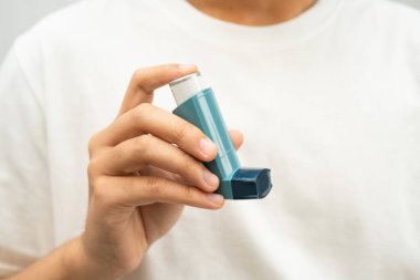 Astım ve kronik obstrüktif akciğer hastalığı COPD, Asyalı genç adam ölçülü doz solunum cihazı kullanıyor..