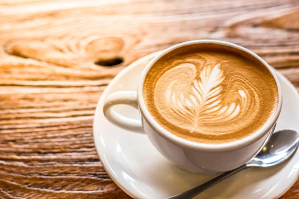 Taza de café arte latte con cuchara y plato en la corteza marrón hermoso fondo textura con luz cálida — Foto de Stock