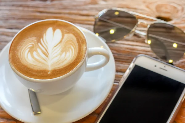 Taza de café arte latte con cuchara y plato en la corteza marrón hermoso fondo textura con luz cálida decorada con gafas de sol — Foto de Stock