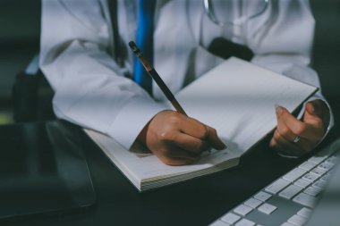 Two doctors and a female nurse meet at a table in the hospital, collaborating on medical tasks using laptops and computers