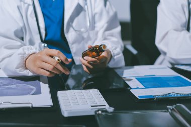 Two doctors and a female nurse meet at a table in the hospital, collaborating on medical tasks using laptops and computers