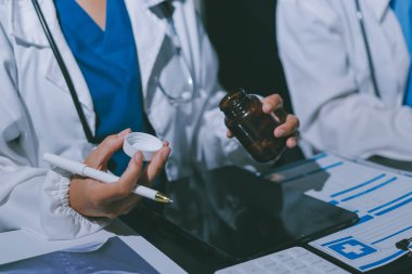 Two doctors and a female nurse meet at a table in the hospital, collaborating on medical tasks using laptops and computers