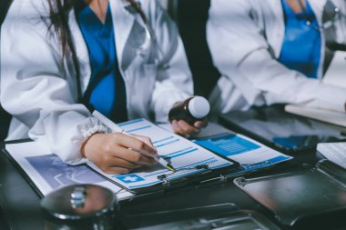 Two doctors and a female nurse meet at a table in the hospital, collaborating on medical tasks using laptops and computers