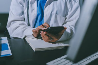 Two doctors and a female nurse meet at a table in the hospital, collaborating on medical tasks using laptops and computers