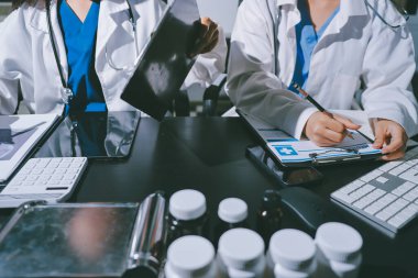 Two doctors and a female nurse meet at a table in the hospital, collaborating on medical tasks using laptops and computers