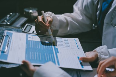 Two doctors and a female nurse meet at a table in the hospital, collaborating on medical tasks using laptops and computers