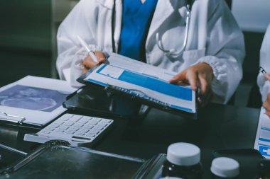 Two doctors and a female nurse meet at a table in the hospital, collaborating on medical tasks using laptops and computers
