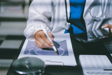 Two doctors and a female nurse meet at a table in the hospital, collaborating on medical tasks using laptops and computers