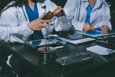 Two doctors and a female nurse meet at a table in the hospital, collaborating on medical tasks using laptops and computers