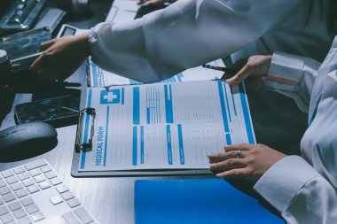 Two doctors and a female nurse meet at a table in the hospital, collaborating on medical tasks using laptops and computers