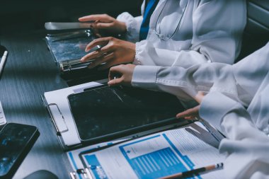 Two doctors and a female nurse meet at a table in the hospital, collaborating on medical tasks using laptops and computers