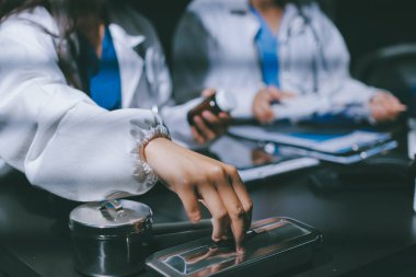 Two doctors and a female nurse meet at a table in the hospital, collaborating on medical tasks using laptops and computers