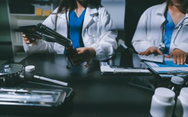 Two doctors and a female nurse meet at a table in the hospital, collaborating on medical tasks using laptops and computers