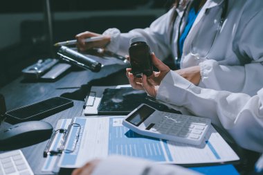 Two doctors and a female nurse meet at a table in the hospital, collaborating on medical tasks using laptops and computers