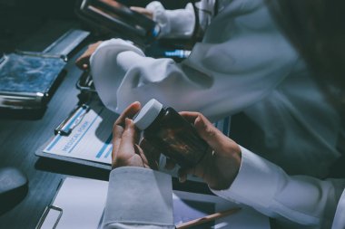 Two doctors and a female nurse meet at a table in the hospital, collaborating on medical tasks using laptops and computers