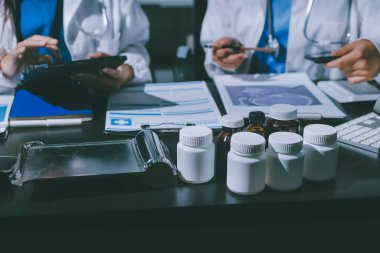Two doctors and a female nurse meet at a table in the hospital, collaborating on medical tasks using laptops and computers