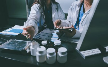 Two doctors and a female nurse meet at a table in the hospital, collaborating on medical tasks using laptops and computers