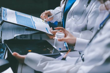 Two doctors and a female nurse meet at a table in the hospital, collaborating on medical tasks using laptops and computers