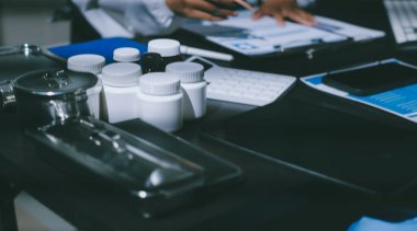 Two doctors and a female nurse meet at a table in the hospital, collaborating on medical tasks using laptops and computers