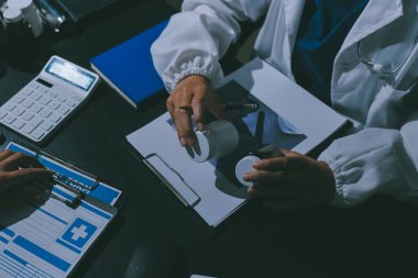Two doctors and a female nurse meet at a table in the hospital, collaborating on medical tasks using laptops and computers