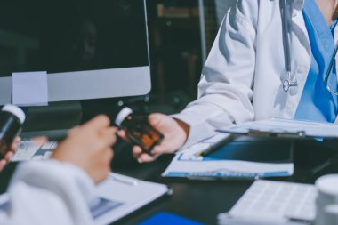 Two doctors and a female nurse meet at a table in the hospital, collaborating on medical tasks using laptops and computers