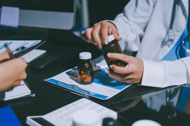 Two doctors and a female nurse meet at a table in the hospital, collaborating on medical tasks using laptops and computers