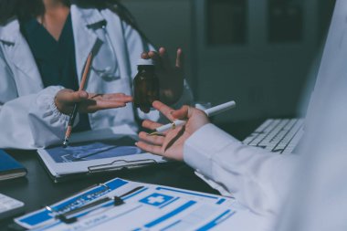 Two doctors and a female nurse meet at a table in the hospital, collaborating on medical tasks using laptops and computers