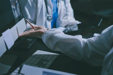 Two doctors and a female nurse meet at a table in the hospital, collaborating on medical tasks using laptops and computers