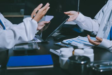 Two doctors and a female nurse meet at a table in the hospital, collaborating on medical tasks using laptops and computers