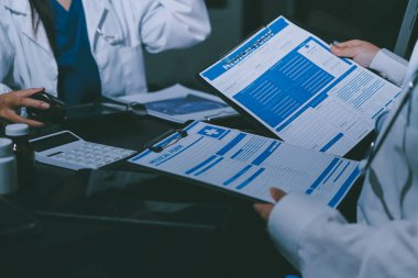 Two doctors and a female nurse meet at a table in the hospital, collaborating on medical tasks using laptops and computers
