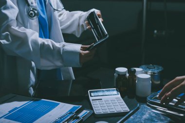 Two doctors and a female nurse meet at a table in the hospital, collaborating on medical tasks using laptops and computers