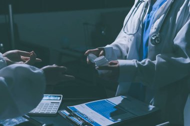Two doctors and a female nurse meet at a table in the hospital, collaborating on medical tasks using laptops and computers
