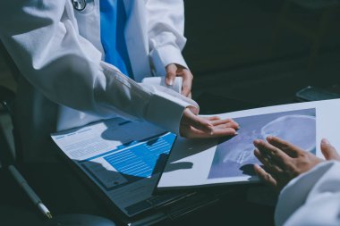 Two doctors and a female nurse meet at a table in the hospital, collaborating on medical tasks using laptops and computers